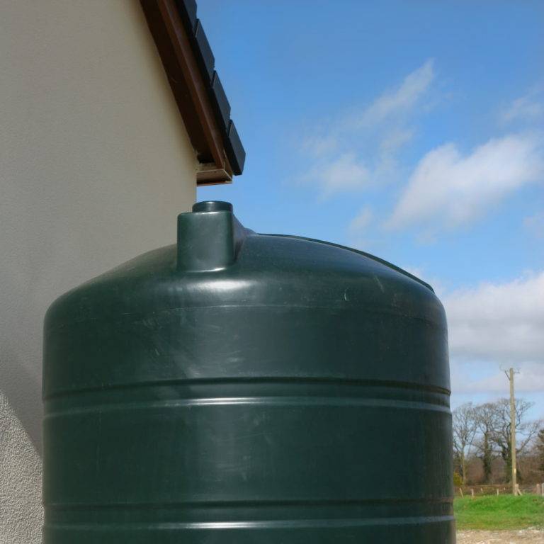 Green plastic diesal tank standing on a bed of concrete at the side of a house.